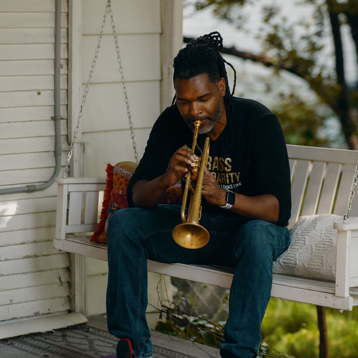 Butchy Austin playing his trumpet outside on a bench swing