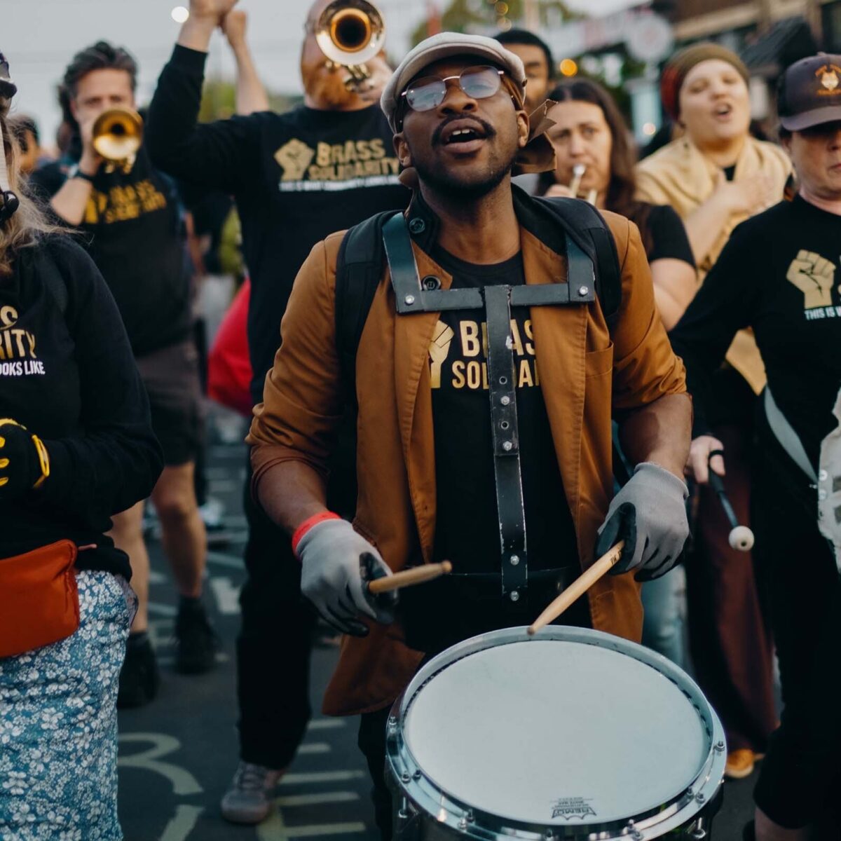 Man drumming outside with fellow Brass Solidarity musicians