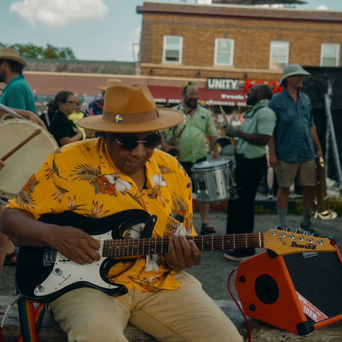 Man in colorful shirt and hat playing guitar at George Floyd Square