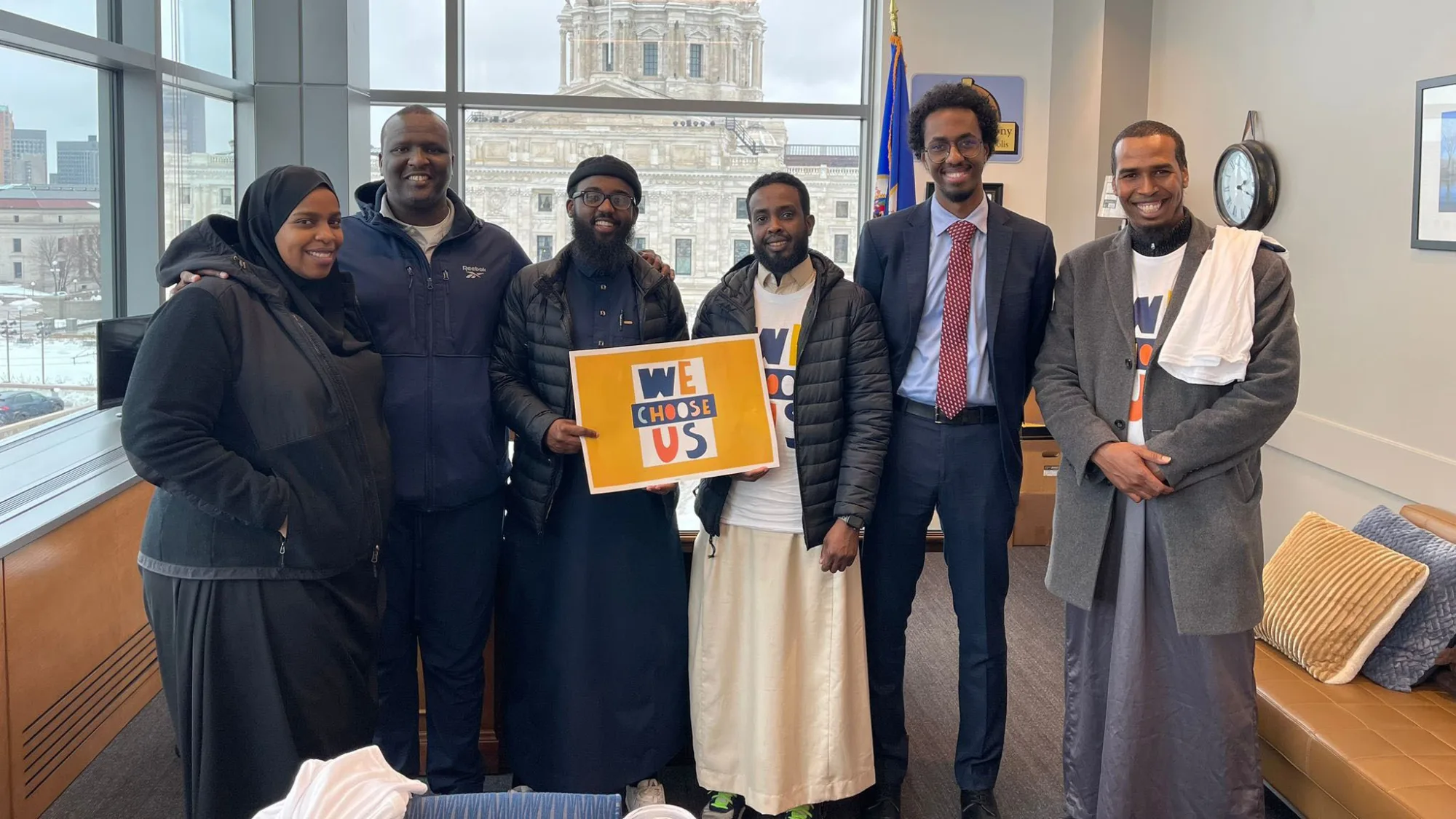 Group of people at the Capitol with signs reading We Choose Us