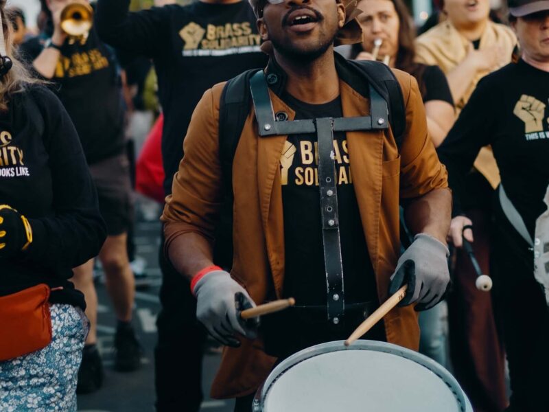 Man drumming outside with fellow Brass Solidarity musicians